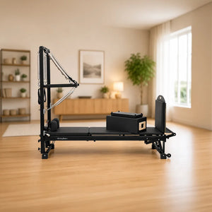 A black  Eleno Pilates reformer machine with a wooden chest plate and adjustable straps, set in a bright, modern home gym with light wood floors and neutral walls.